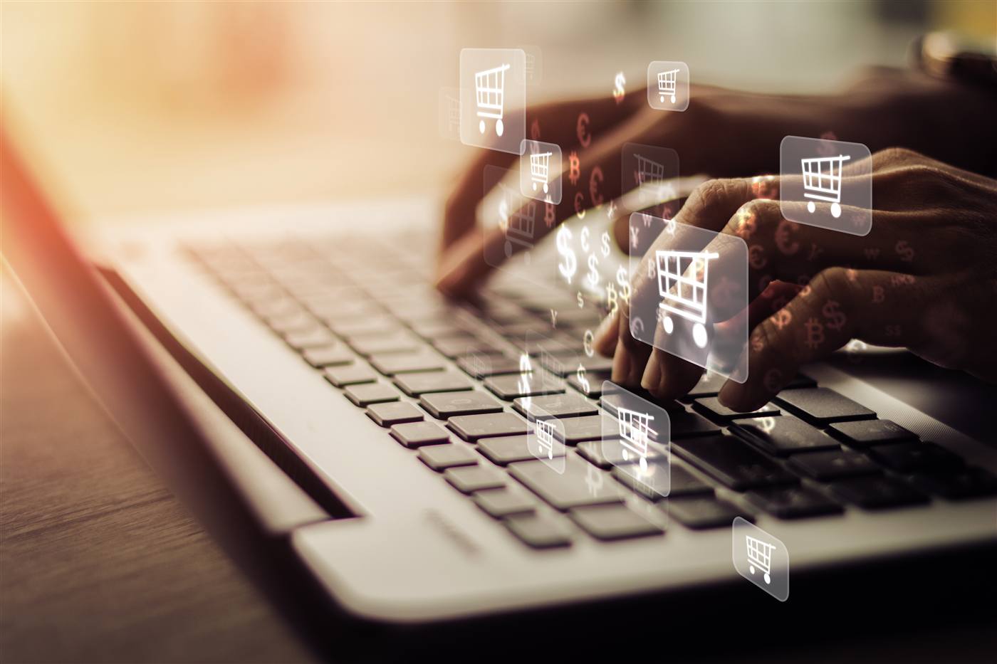 Hands typing on a laptop keyboard with floating shopping trolley, dollar, euro and Bitcoin icons above.