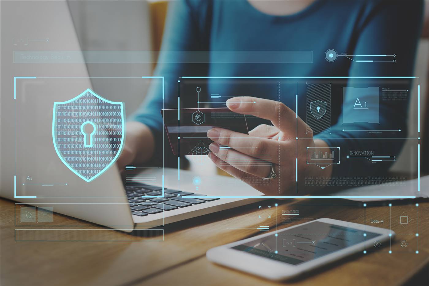 Person holding a payment card before an open laptop with a digital security HUD overlay showing padlock and data graph icons.