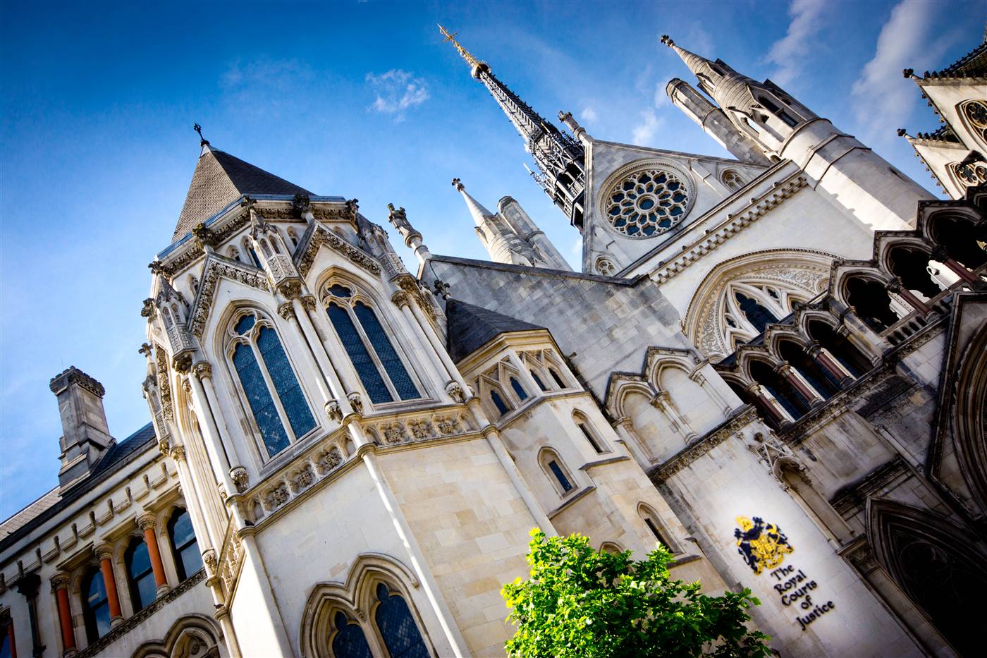 Low-angle view of the Royal Courts of Justice showing neo-Gothic stone spires, tracery windows and a carved Royal Crest.